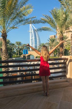 Dubai, Birleşik Arap Emirlikleri - 12 Kasım 2018: Burj al Arab Madinat Jumeirah genç turist kadın tarafından görülen eller havada küçük alışveriş torbaları, Dubai holding ile kırmızı elbise giymiş