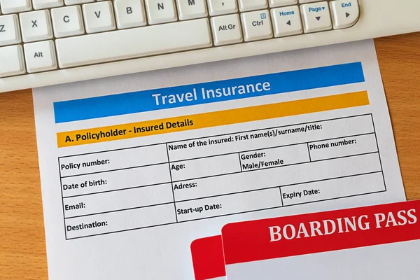 Travel insurance form on wooden table with boarding pass ticket and keyboard. Agencies sell airplane tickets or travel packages and allow consumers to purchase travel insurance as an added service.