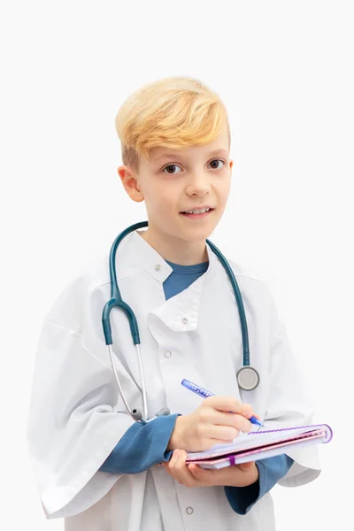 愉快的男孩穿他的父亲医疗制服演奏医生与听诊器在脖子附近写处方查出在白色背景 未来一代希望成为新职业医生的孩子的概念 — 图库照片