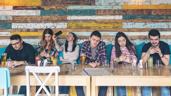 Group of friends using smartphone at rustic restaurant, Young hipster people addicted by mobile phone on social network community, Technology concept with always connected millennials