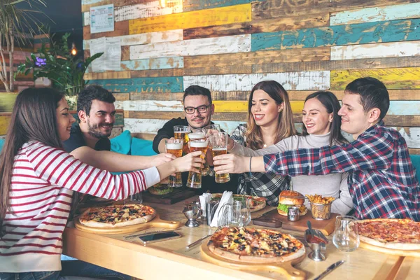 Dostluk kavramı ile birlikte vaktinizi ve rustik pizzacıda gerçek eğlenmek gençler pizza ve hamburger, Restoran bar yemek bira ile kızartma tarafından kutluyor mutlu genç hipster arkadaş, alkış