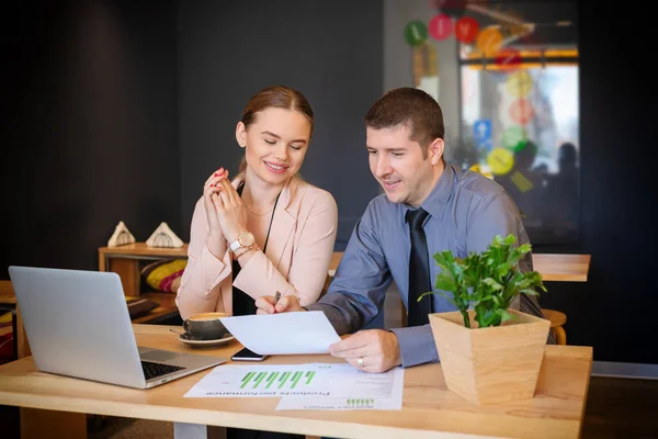 Konuşmak ve modern kafede belgelerini görüntüleme iki genç iş adamları. İşadamı finansal verileri analiz toplantı sırasında iş işkadını meslektaşı ile tartışırken dizüstü bilgisayar ile.
