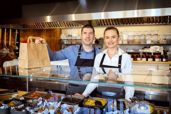 Küçük işletme sahibi içinde eatery, tezgahın arkasındaki holding gıda sipariş eve teslim için önlük çalışan başarılı genç garsonlar gülümseyen portresi