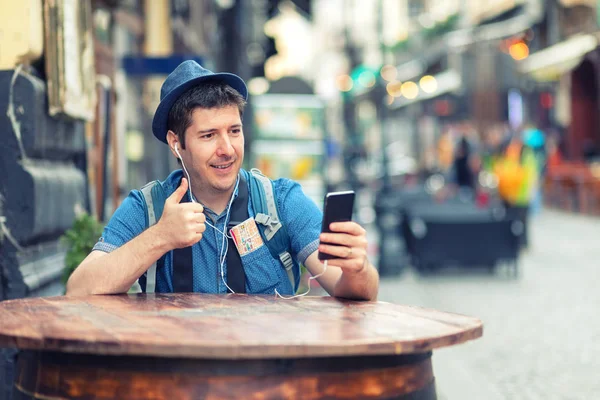 Traveler with trendy look having a video call showing thumb up while enjoy exploring streets of big cities, Young man enjoying city vibes, tourist sharing experience with friends on social media