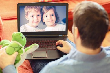 Rear view of dad relaxing on couch while talking to his children using laptop at home, Mature man father lying on sofa and communicate trough video call on laptop with his kids, a little boy and girl showing them toys clipart