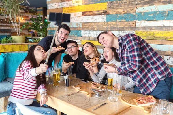 Komik yüzlerle öğle yemeği partisinde selfie çeken en iyi arkadaşlar, genç trendy insanlarla mutlu arkadaşlık konsepti birlikte bira içmek ve bar restoranda pizza paylaşımı