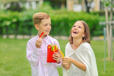 Mutlu çocuklar doğada taze sebze yeme - gülümseyen çocuklar patates kızartması şeklinde dilimlenmiş renkli biyo biber paylaşımı - küçük erkek ve kız açık vitamin dolu sağlıklı atıştırmalık tutarak