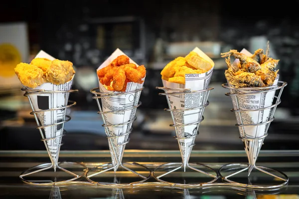 Sea food in cones at counter in smal street shop in Spain, snack with mixed takeaway grilled fish and fried seafood, delicious roasted octopus, anchovies and calamari ready to eat by tourists