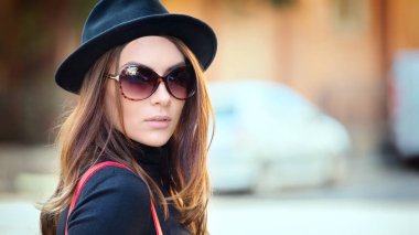 Şık siyah şapka ve büyük retro güneş gözlüğü giyen gülümseyen genç kadının açık moda portresi, küçük Italyan kasabasının sokaklarında mutlu trendy kız closeup