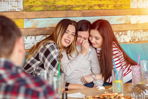 Friends comforting and consoling crying young woman - friendship concept with young millennial girls at restaurant group meeting supporting social problems and depression of their friend, relationship problems of teens