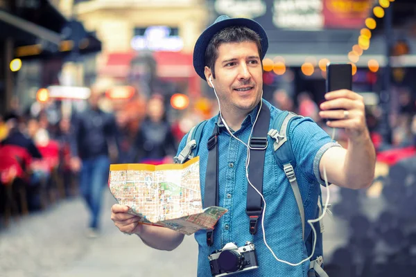 Smiling man tourist in London taking a selfie on crowded streets full of pubs, Happy middle aged male holding city map vlogging and sharing content live on social media network from eurotrip