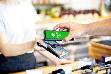 Garson mağazada akıllı telefon ile ödeme adam için kart okuyucu tutan, Müşteri ödeme için cep telefonu kullanarak, kasiyer nfc teknolojisi üzerinden işlem kabul ile küçük işletme hizmet kavramı.