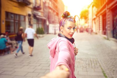 Mutlu rahat hipster kız şehir caddesinde yürürken arkalarına bakarak el tutarak - kulaklık ile genç kadın eğlenceli seyahat sahip - gülümseyen funky kız arkadaşı kameraya bakarak erkek arkadaşı çekerek