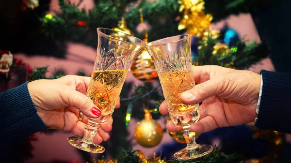 Senior couple hands celebrating Christmas toasting champagne wine at home with decorated Christmas tree in background - winter holiday concept with people cheering