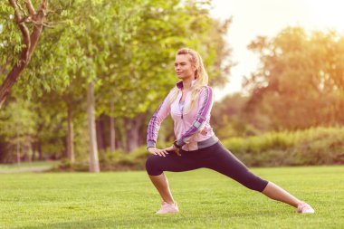 Genç kadın germe ve gün batımı sırasında parkta ısınma - güzel kız sonbaharda fitness önce bacaklar germe - jogger kışın açık koşu egzersiz yapıyor