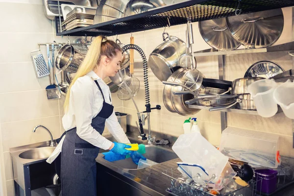 İş gününün sonunda lavaboda bulaşık yıkama küçük restoran Şefi - mutfak işçisi bulaşıkları temizlemek için sünger kullanarak - eatery mutfakta iş başında genç kadın