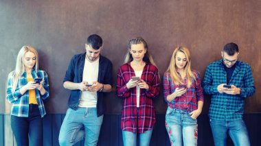Üniversite molasında akıllı telefonu duvara karşı kullanan bir grup arkadaş - cep telefonu bağımlısı genç hipster insanlar - online bağlantılı milenyum teknolojisi kavramı