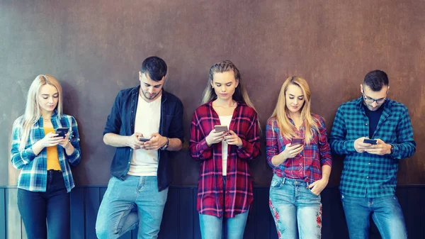 Üniversite molasında akıllı telefonu duvara karşı kullanan bir grup arkadaş - cep telefonu bağımlısı genç hipster insanlar - online bağlantılı milenyum teknolojisi kavramı