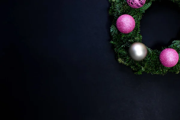 Black promotional backgroud with christmas ornaments, fresh, green wreath, pink and white baubles