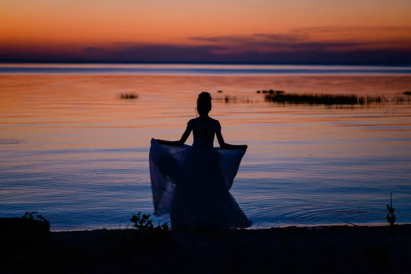 The bride dances against the lake at sunset. The dress is spinning