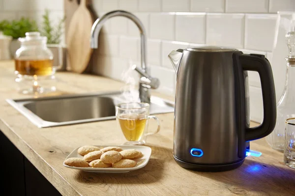 Electric kettle with tea and cookies in the kitchen interior