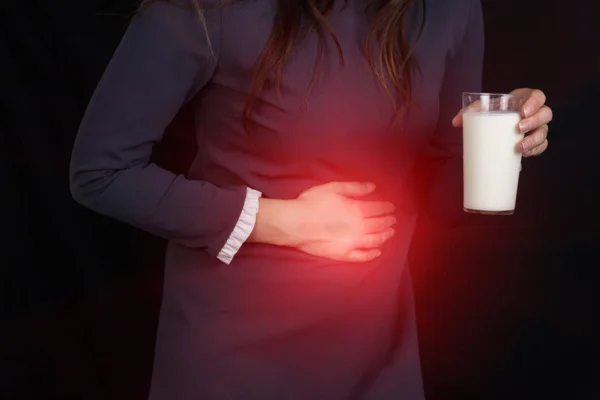 Девушка на черном фоне держит в руке стакан молока, изжогу, боль в животе, крупным планом — стоковое фото