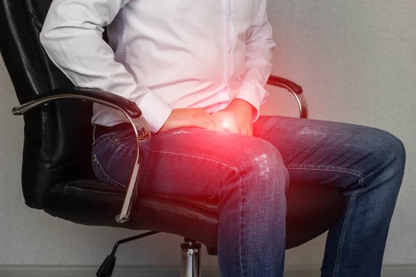 Bir adam bir ofis koltuğu oturur ve kasık, kasık, prostatit için tutar