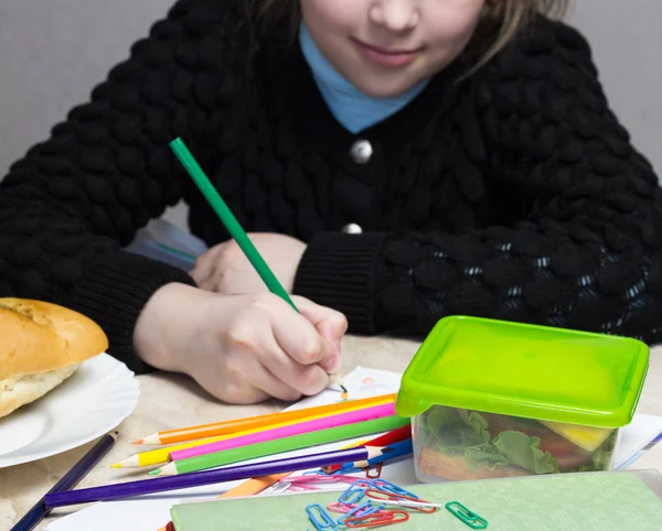 Het meisje doet de lessen, op tafel ligt een sandwich, fruit, noten, schoolboeken, potloden, nosh — Stockfoto