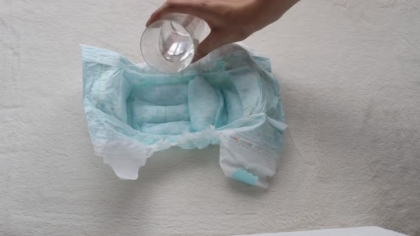 Flickan häller vatten från ett glas till en baby blöja och torkar en servett, närbild, blöjor och vatten — Stockvideo