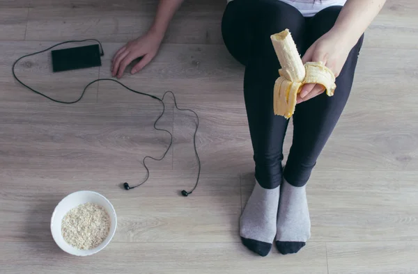 Una chica en alce negro comiendo un plátano, un teléfono con auriculares, avena — Foto de Stock