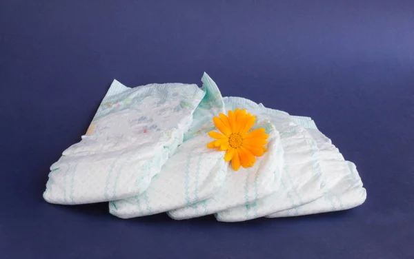 Fraldas para bebês em um fundo azul e uma flor de laranja em fraldas — Fotografia de Stock