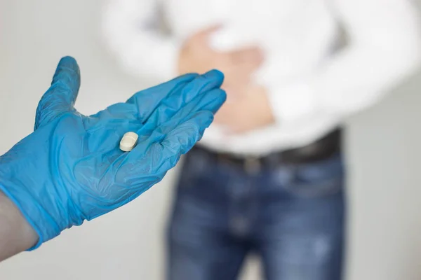 man holds on to stomach, abdominal pain, hand in glove with a pill, close-up, gastritis