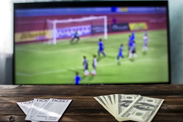 On the TV is football on the table are betting tickets and money dollars, sports bets, gain