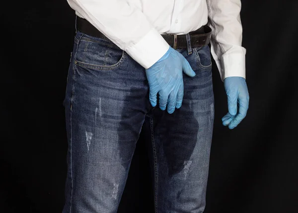 De man houdt vast aan het perineum, de lies in de medische handschoen, natte broek, prostatitis, mannelijke problemen — Stockfoto