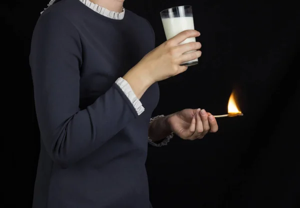 La fille sur un fond noir tient une allumette brûlante et boit du lait, des brûlures et des douleurs dans l'estomac, des brûlures d'estomac et du lait — Photo