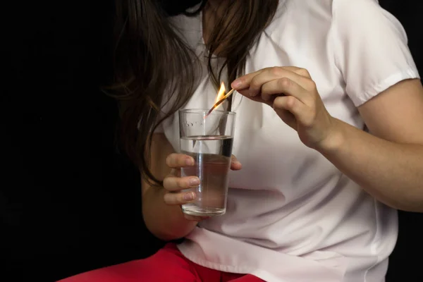 在黑色背景的女孩拿着一杯水 熄灭燃烧的火柴 疼痛和燃烧的胃 胃灼热 — 图库照片