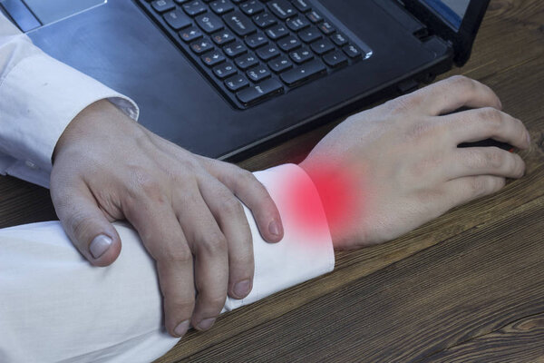 Человек работает за компьютером и держит его за руку, его рука болит, туннельный синдром
