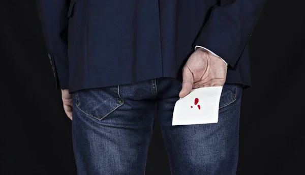 Homme en costume tient du papier toilette avec du sang, hémorroïdes, fond noir, piles — Photo