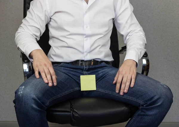 A man is sitting in an office chair, on the crotch and groin is glued a sticker, a close-up, a place for an inscription — Stock Photo, Image