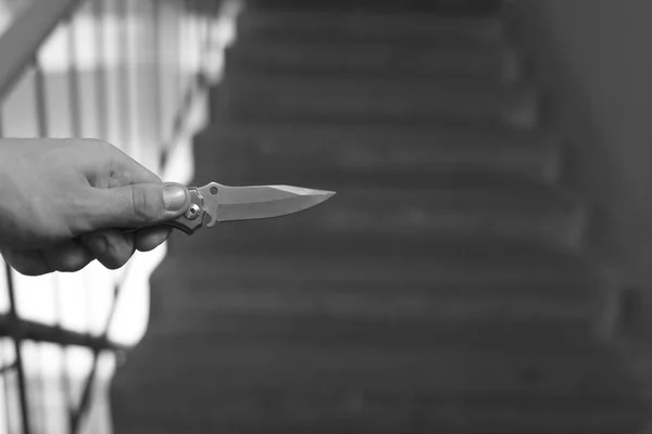 La mano de un hombre con un cuchillo contra el telón de fondo de una escalera en la entrada, asesinato, asalto —  Fotos de Stock