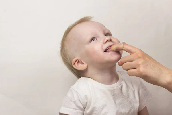 Mała dziewczynka aż rok, gryzie jej matka przez palec, który czyści jej zęby, zbliżenie, białe tło — Zdjęcie stockowe