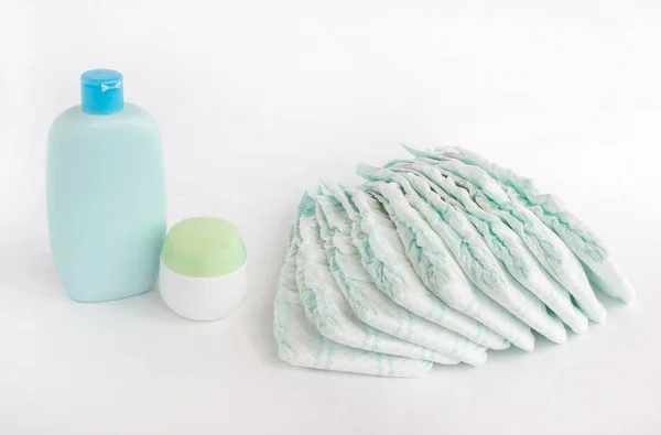 Pañales para bebés sobre fondo blanco y champú y crema para bebés —  Fotos de Stock