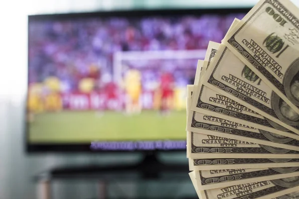 Dollars against the backdrop of a TV set for football, football and money — Stock Photo, Image