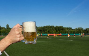 Bir adamın elinde bir bardak bira nerede futbol, yakın çekimler oynamak bir futbol stadyumu arka planı tutar.