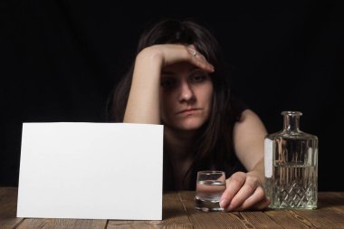 Onun eli, şişe ve alkol, siyah arka plan, temiz bir sayfayla bir cam ile oturan üzgün kız