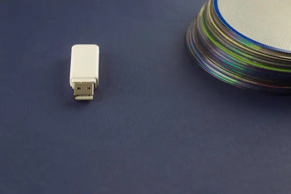 White flash drive and a stack of CD, DVD, computer, storage