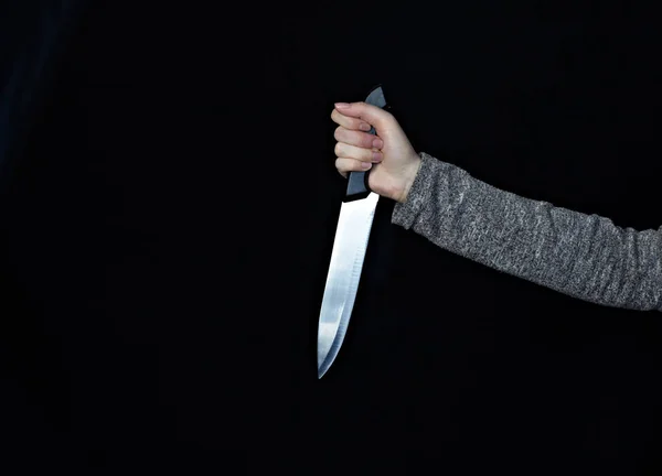 Hand of a girl with a knife on a black background, close-up