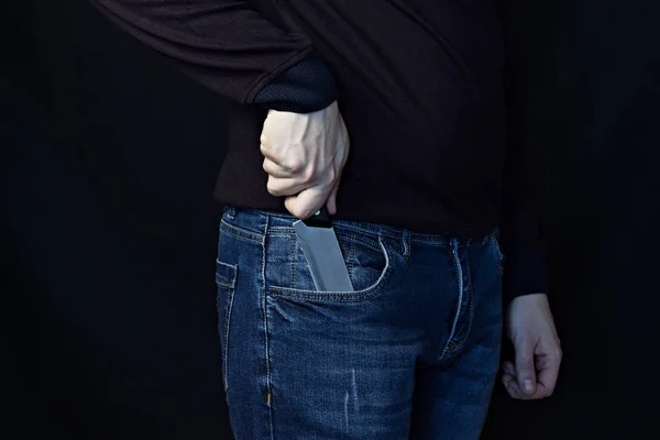 Un homme sort un couteau de son pantalon, un fond noir — Photo