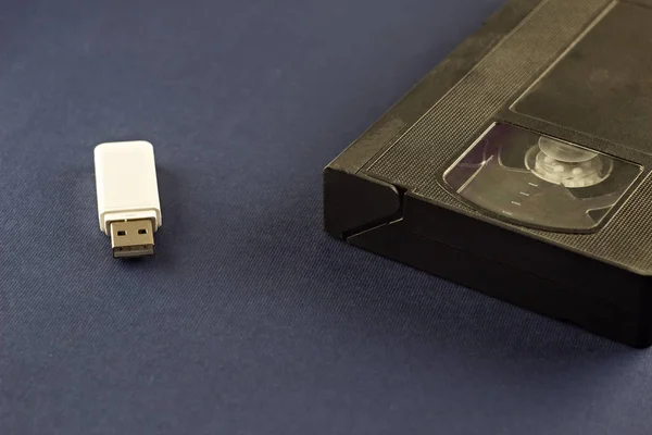A white flash drive on a blue background and a video cassette