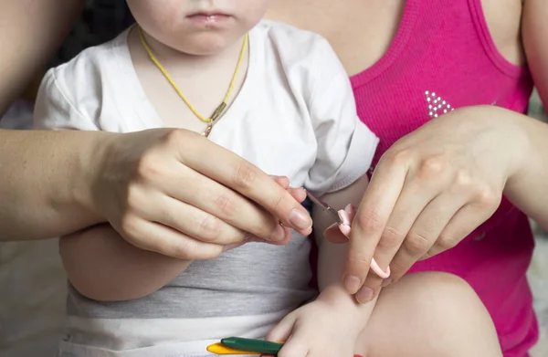 女の子は母親が少女の手に彼女の爪をカットします。 — ストック写真